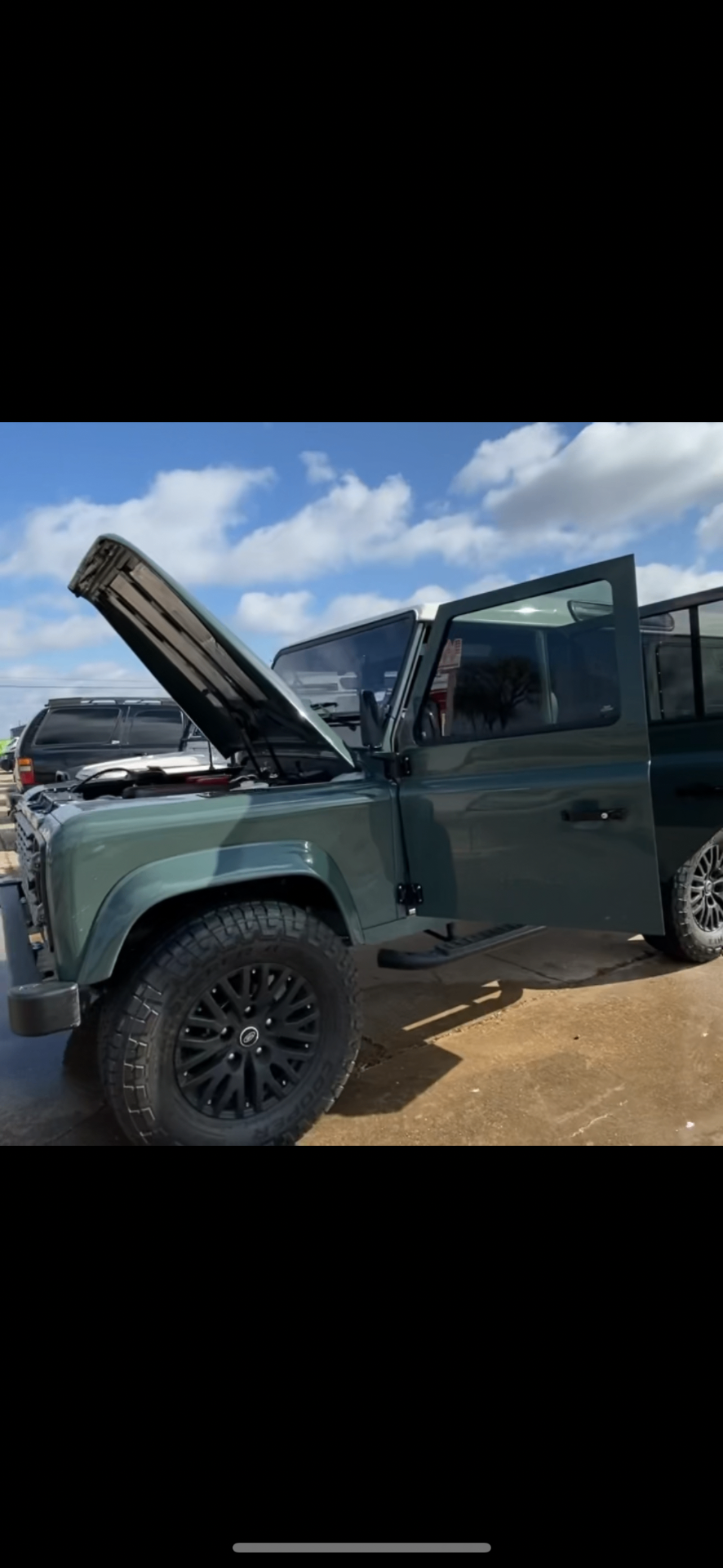 Keswick green Defender 110 with hood open and door ajar outside the shop