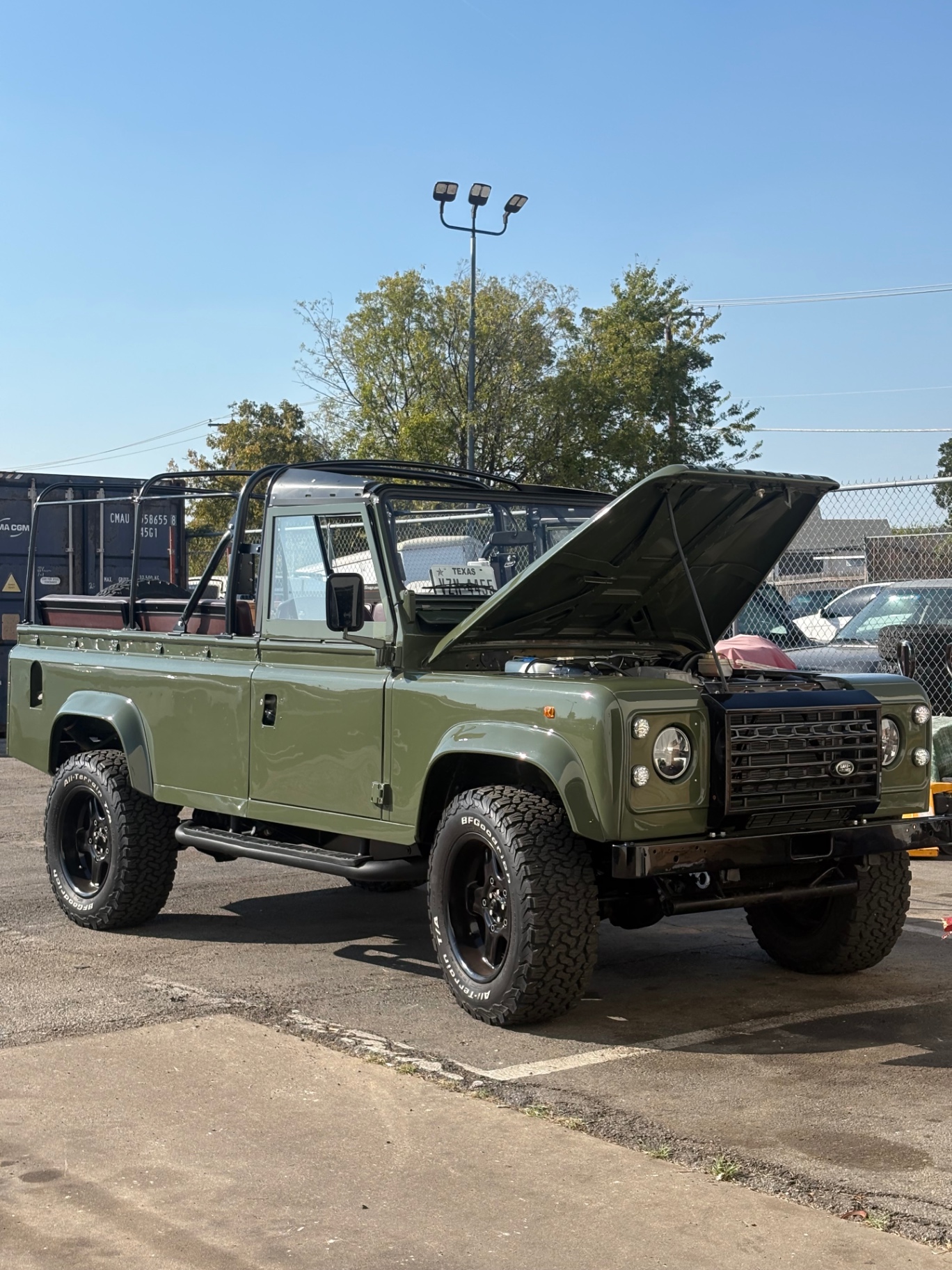 Olive green open-air Defender 110 with roll cage and hood open