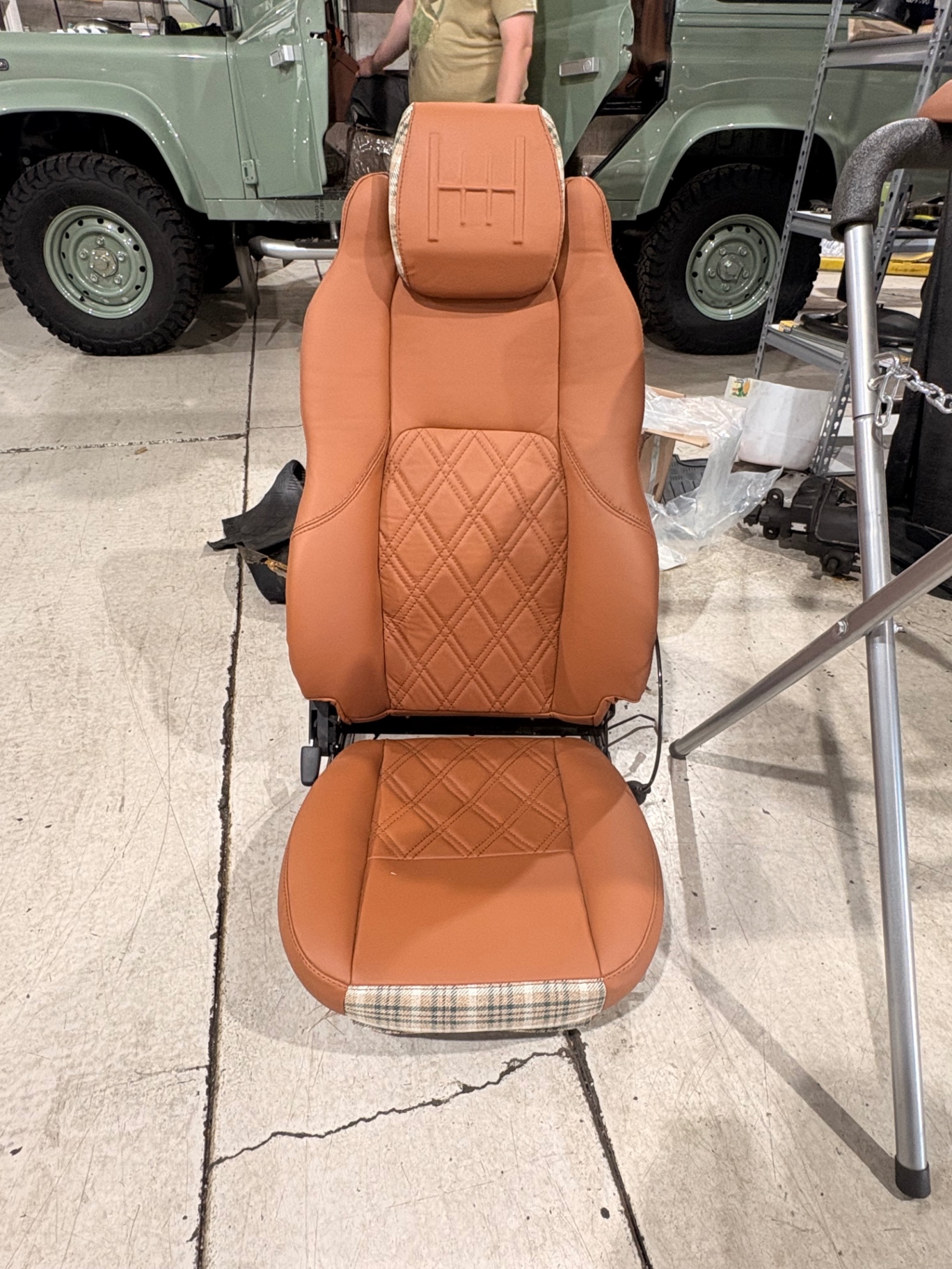 Tan diamond-stitched leather Defender seat with H-pattern embossed headrest and plaid trim