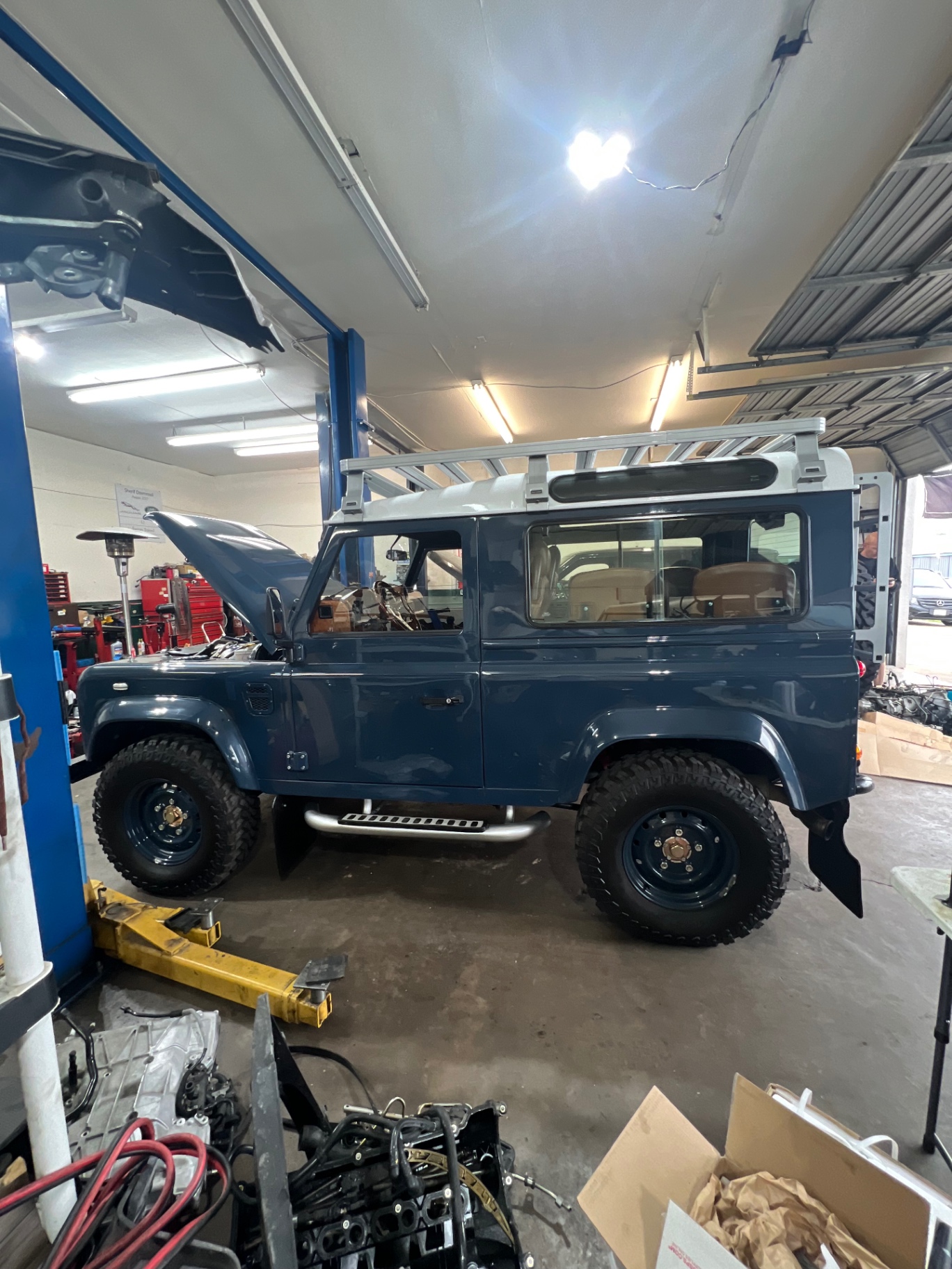 Marine blue Defender 90 with roof rack and hood open inside the shop