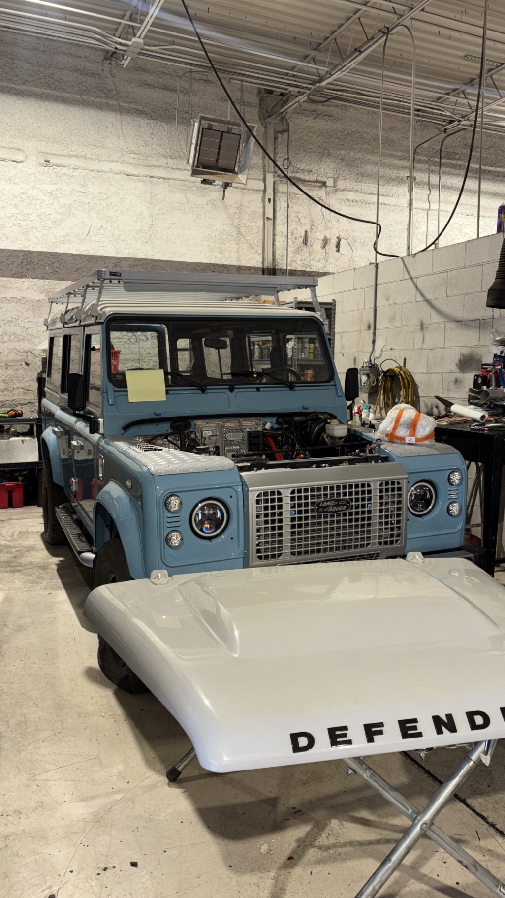 Sky blue Defender 110 in assembly with grille and hood off inside the shop