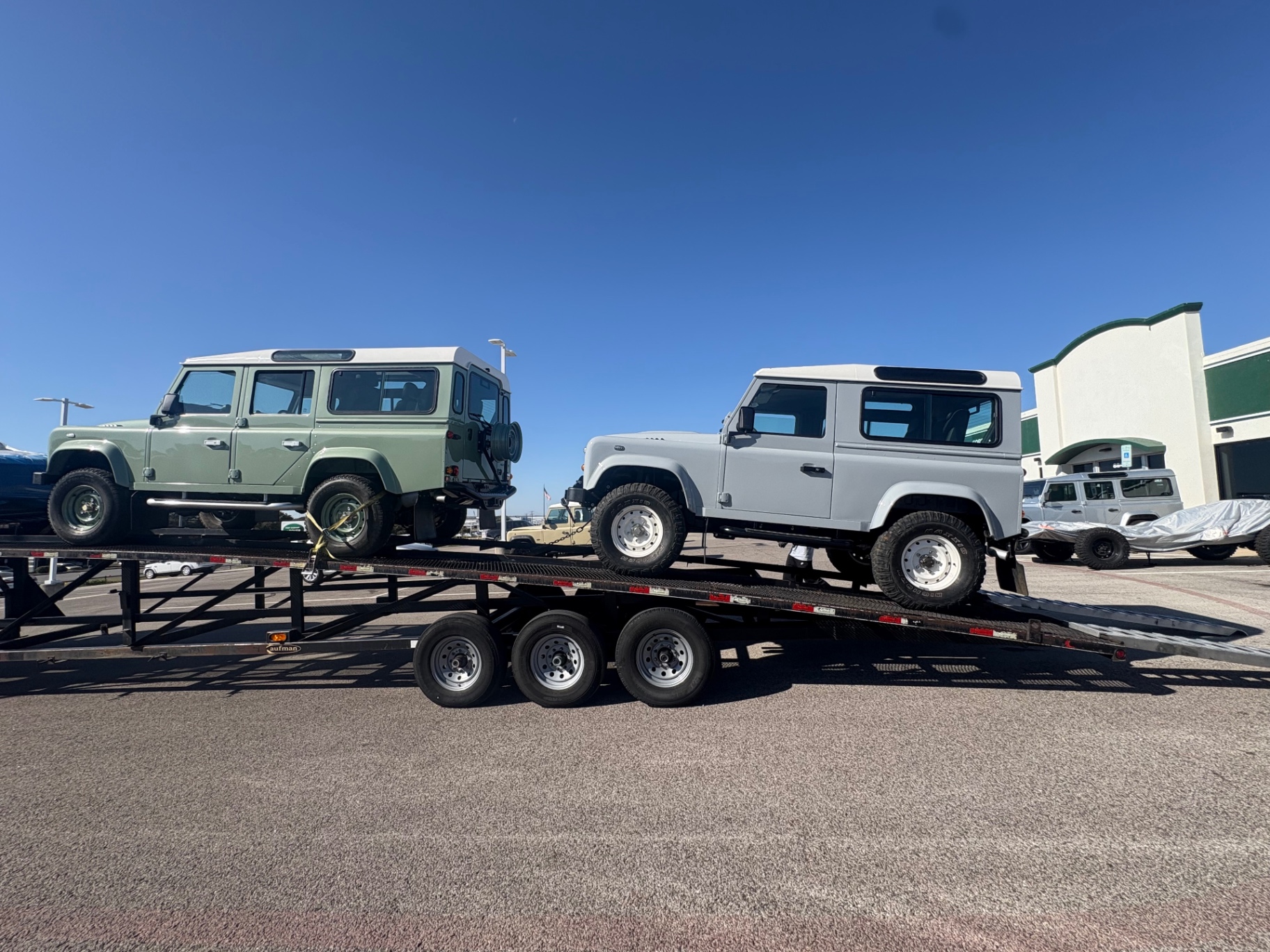 Two custom Defenders loaded side-by-side on a trailer leaving the Fort Worth Rover shop