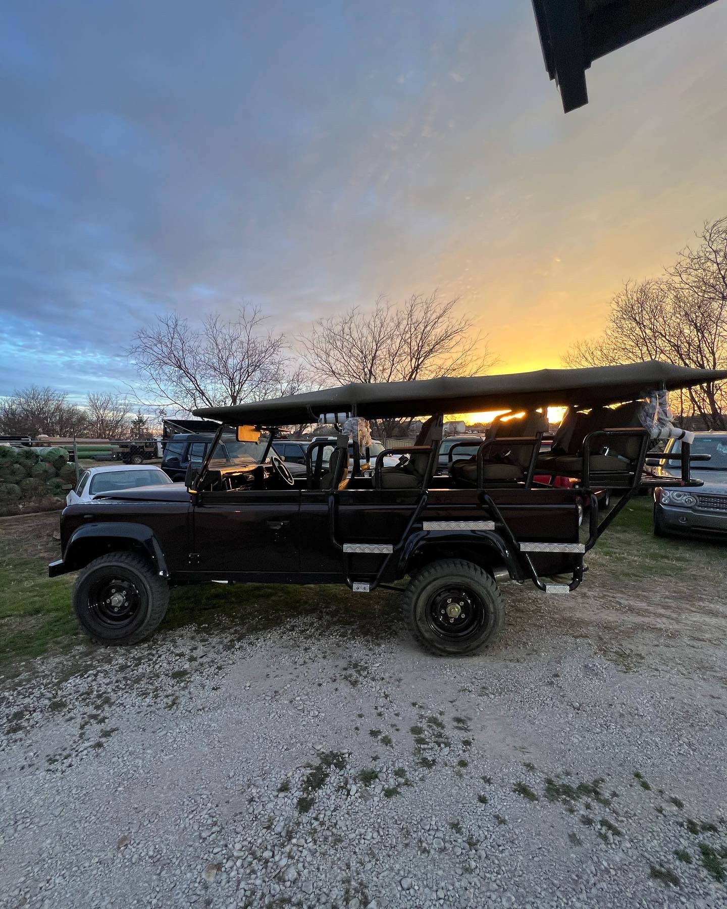 Black open-top Defender 110 safari with bench seating at sunset