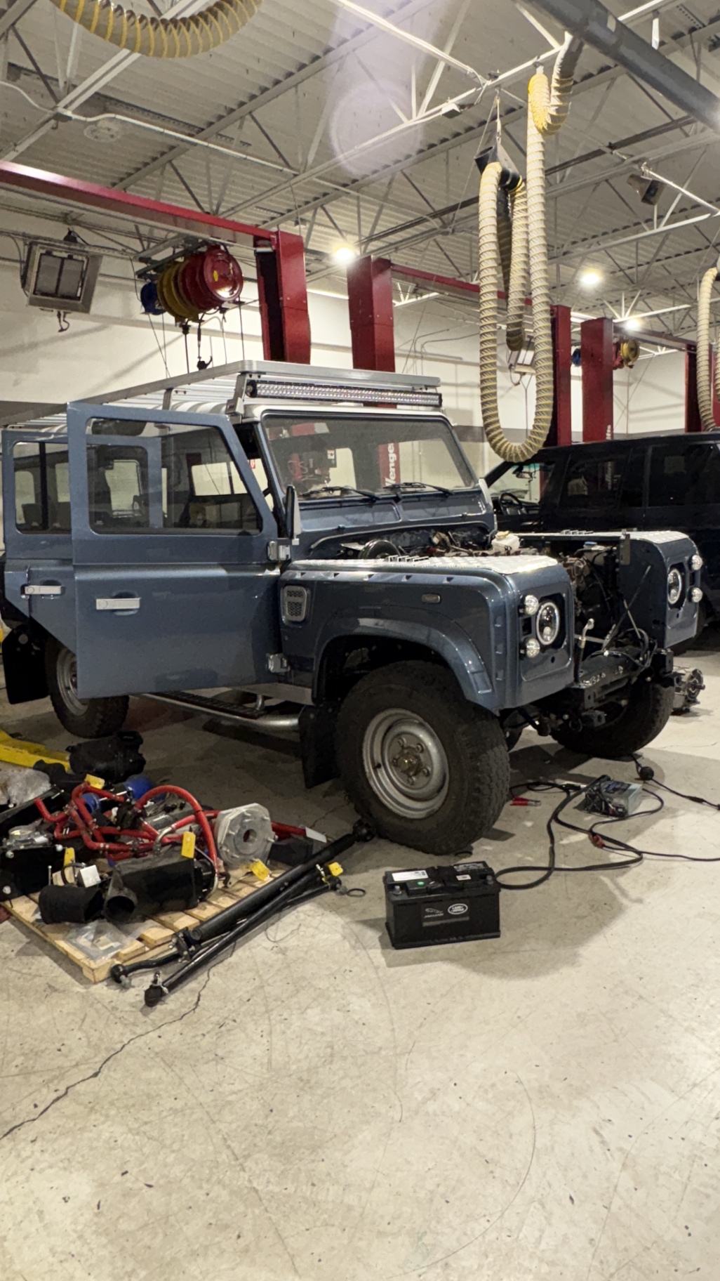 Blue Defender 110 in the workshop surrounded by suspension and driveline parts