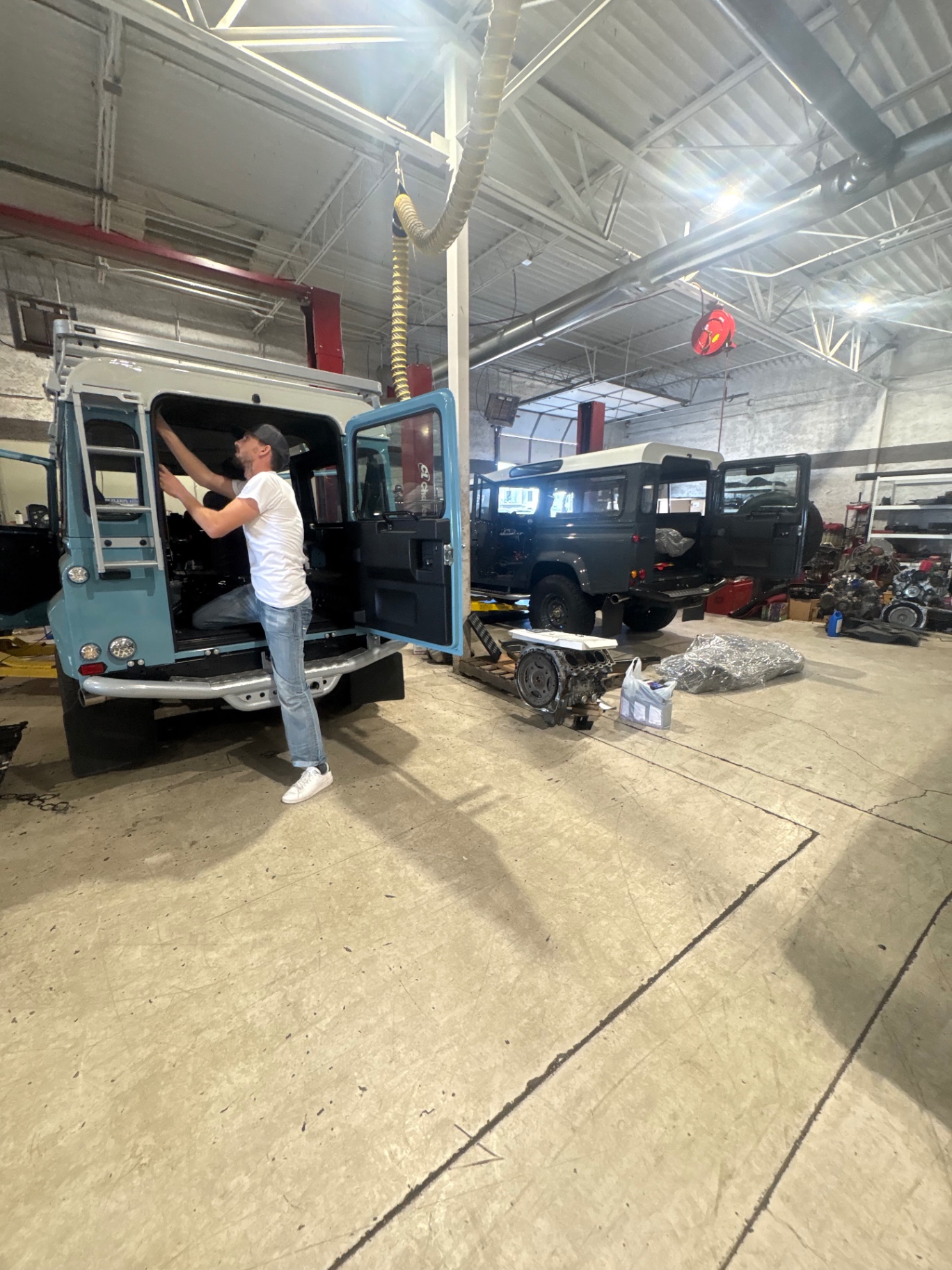 Technician working inside a sky blue Defender build while another truck sits in the background